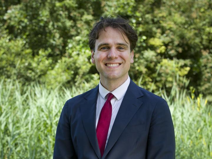 Wethouder Marijn van Ballegooijen lacht in camera met groene achtergrond