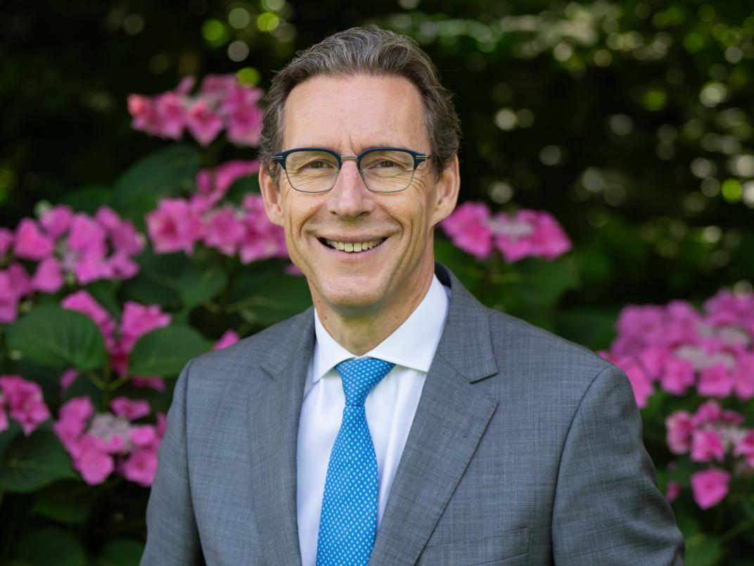 Portretfoto burgemeester Tjapko Poppens bij paarse bloemen