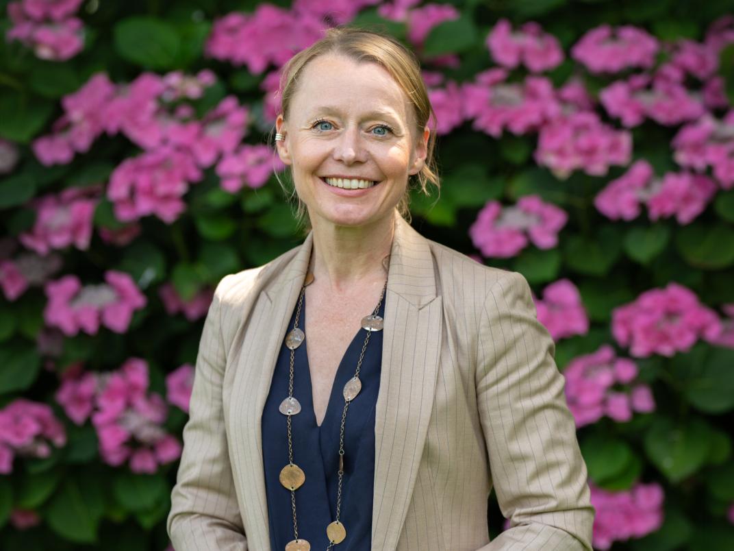 Profielfoto van wethouder Floor Gordon in cremekleurig kostuum voor een struik met roze bloemen
